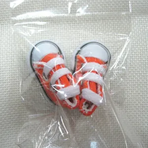 Close-up of miniature 3.5cm orange canvas doll shoes inside clear plastic packaging.