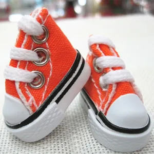 Close-up of miniature 3.5cm orange canvas doll shoes with white laces and rubber soles.