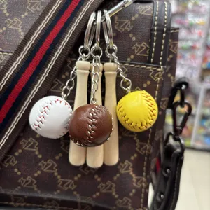 Detailed view of handmade mini baseball and wooden bat keychains on a textured bag