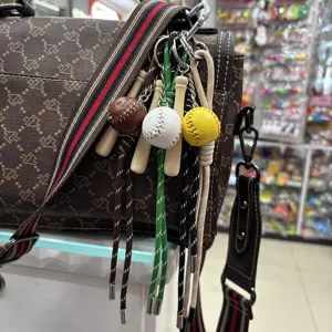 Detail shot of baseball and wooden bat keychains hanging on a brown bag strap.