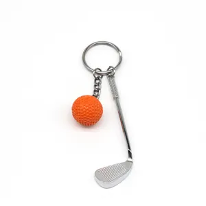 Detailopname van een creatieve golfclub-sleutelhanger met een oranje bal in glanzend metaal
