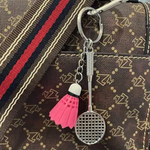 Detail van roze shuttle en zilveren metalen racket sleutelhanger op een tas met textuur.