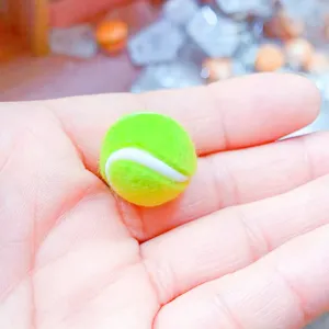 Makro-Nahaufnahme des 2 cm großen Mini-Tennisball-Anhängers auf der Hand