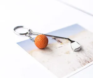 Detailopname van een oranje golfbal en zilveren club sleutelhanger op een ansichtkaart