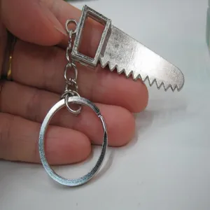 Detailed view of a miniature metal saw keychain held in hand for scale