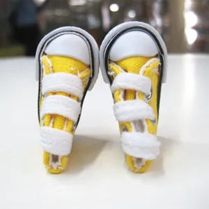 Close-up of mini 3.5cm yellow canvas doll shoes with white laces and toe cap.