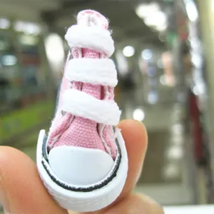 Detailed close-up view of a mini 3.5cm pink canvas doll shoe held between fingers for scale