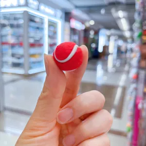 Detailaufnahme eines roten Mini-Tennisballs, der von Fingerspitzen gehalten wird