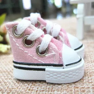 Close-up of mini pink 3.5cm canvas doll shoes with white laces and rubber soles.