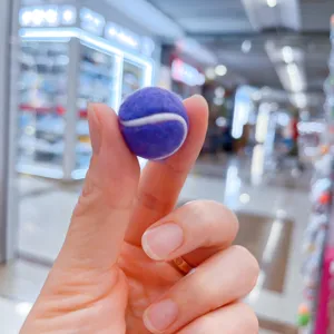 Nahaufnahme eines violetten Mini-Tennisball-Anhängers, der zwischen Fingern gehalten wird