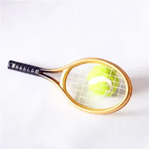 Primo piano di una mini racchetta da tennis dorata e pallina gialla per portachiavi.