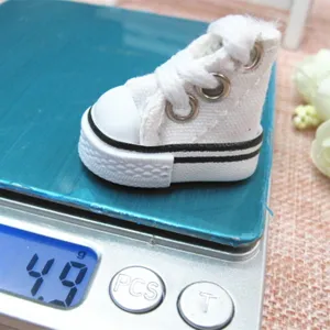 Close-up of a 3.5cm miniature white canvas doll shoe weighing 4.9g on a digital scale.
