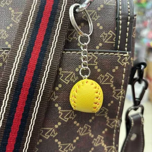 Mini yellow leather baseball keychain 2cm sports pendant hanging on a brown handbag