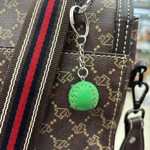 Detailed mini green baseball keychain with red stitching hanging on a patterned leather bag