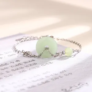 Gros plan d'un bracelet en jade Ping'an Kou vert pâle avec chaîne en argent et breloque Fu.