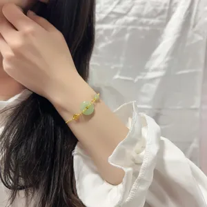 Gros-plan d'un délicat bracelet en or avec pierre de jade verte et pendentif Fu au poignet