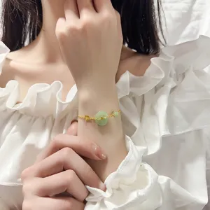Détail d'un bracelet doré délicat orné d'un pendentif en jade Hetian vert style ping'an kou