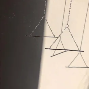 Detail van minimalistische punk oorbellen met zilveren ketting en lange metalen staaf