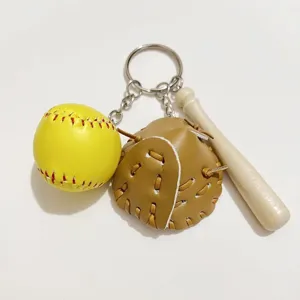 Close-up view of a sports keychain with a yellow baseball, leather glove, and wood bat.