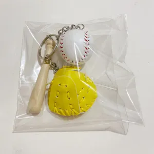 Detailed view of miniature baseball bat and yellow glove keychain set in plastic bag