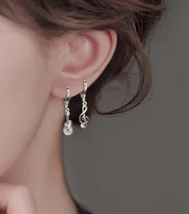 Close-up of asymmetric silver music note and rhinestone guitar earrings worn on ear