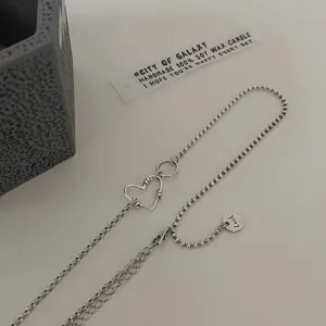 Makroaufnahme einer silbernen Herzkette mit Luck-Anhänger und gemischtem Kugelketten-Design