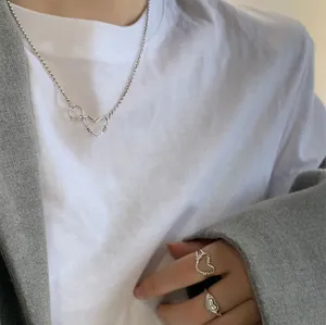 Detailansicht der silbernen Herzenskette und passenden Ringe zu einem grauen Blazer.