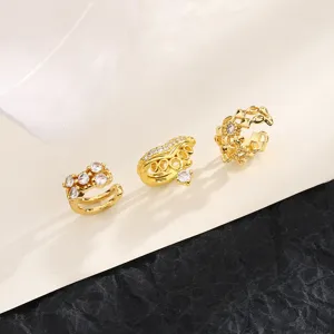Λεπτομερής όψη τριών κομψών χρυσών ear cuff με ζιργκόν σε σχέδιο κορώνας και σταυρού