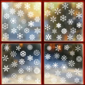 Diversi adesivi statici a fiocco di neve bianchi su un vetro rosso per decoro natalizio.