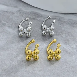Close-up detail of minimalist gold and silver cross-shaped bead ear clips on marble