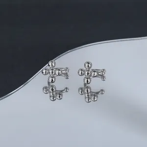 Detailed macro view of minimalist silver cross beaded ear cuffs on a reflective surface