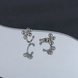Macro view of silver cross bead ear cuffs reflecting on a sleek curved mirror surface