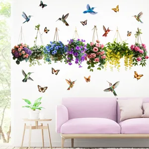 Dettaglio di cesti di fiori sospesi e adesivi murali con colibrì su una parete bianca.