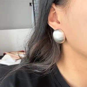 Détail d'une boucle d'oreille ovale minimaliste en argent mat sur l'oreille d'un modèle