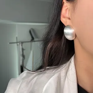 Détail d'une boucle d'oreille ovale en argent brossé mat portée par un mannequin femme