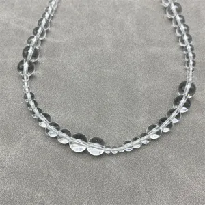 Detail shot of clear quartz crystal beads arranged in varying sizes on a grey mat