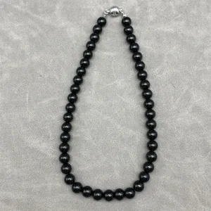 Macro view of a polished black bead necklace with a secure silver magnetic clasp.