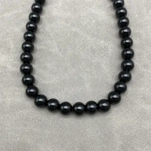 Macro detail of a glossy black bead necklace set against a textured grey background