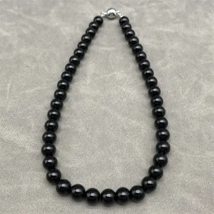 Detailed view of polished black bead necklace with magnetic clasp on grey background.