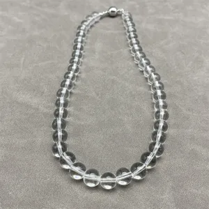Detail of a transparent white crystal bead necklace with a silver magnetic ball clasp.