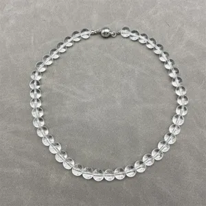 Close-up view of a transparent crystal bead necklace with a silver magnetic clasp on grey.