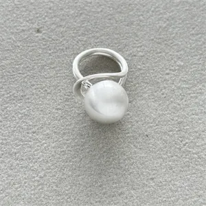 Anillo de plata mate moderno con una gran bola de metal cepillado sobre tela gris.