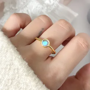 Close-up of a minimalist gold ring with a glowing oval moonstone on a hand.