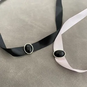 Close-up detail of minimalist black and pink ribbon chokers with oval black stone pendants.