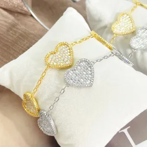Nahaufnahme von mit Zirkonia besetzten Herzanhängern an eleganten gold- und silbernen Armbändern