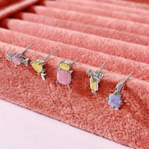 Nahaufnahme bunter Zirkonia-Ohrstecker in Bonbonform auf rosa Samt präsentiert.