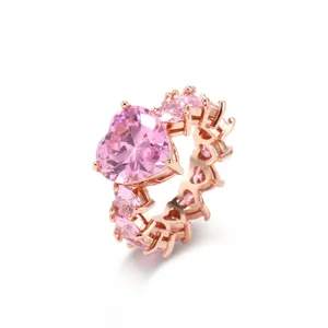 Nahaufnahme eines rotgoldenen Rings mit leuchtend rosa herzförmigen Zirkoniasteinen.