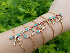 Detailansicht goldener Kettenarmbänder mit bunten Zirkon-Alphabet-Anhängern und Stern