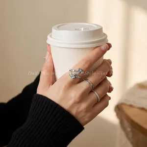 Closeup view of dainty leaf zircon ring and stacked silver bands worn on elegant hands with coffee.