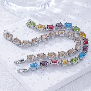Detail of silver bracelets set with colorful oval-cut zircons on a white stone slab